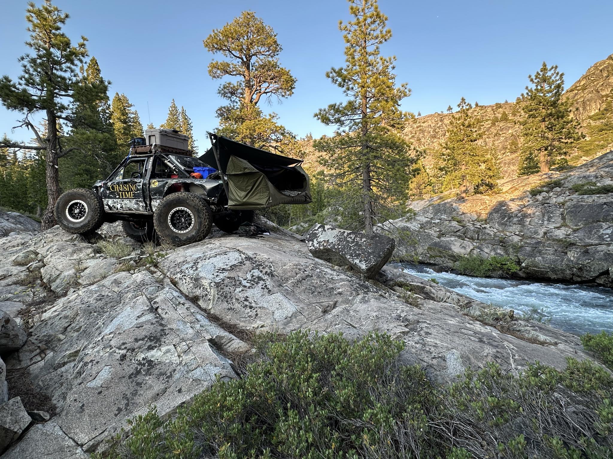 Off-road vehicle on rocky terrain with trees and a river in the background, Mammoth XL Hammock Mount and Haven Safari set up in rear hitch