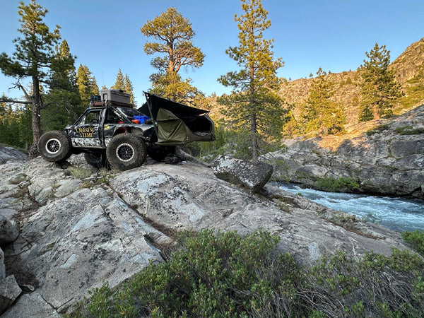 Off-road vehicle on rocky terrain with trees and a river in the background, Mammoth XL Hammock Mount and Haven Safari set up in rear hitch